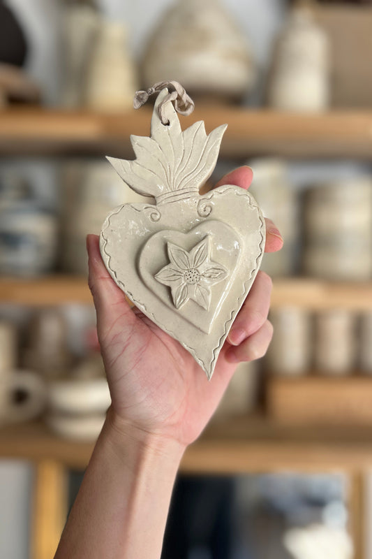 ex voto ou coeur sacré artisanal réalisé en grés il présente une petite fleur en relief tenu dans la main de la céramiste ou l'atelier se situe près de Montpellier